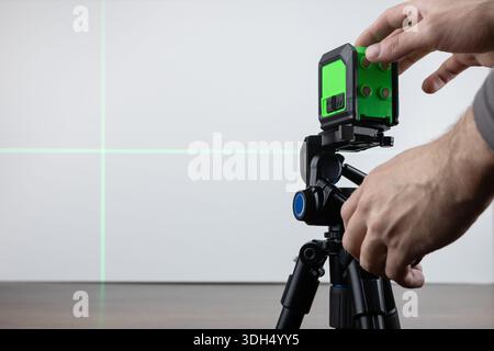 Construction worker is using cross-line laser level meter with line green beam to mark the floor in construction site. Stock Photo