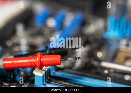 red and black multimeter probe probing electric components on circuit board. Diagnostic testing in technical laboratory setting Stock Photo