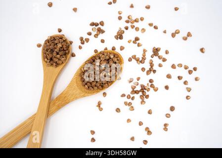 Minimal composition of wooden spoons filled with buckwheat groats scattered on a light background. Healthy food, clean eating and natural grain concep Stock Photo