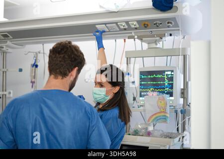 Nurses in scrubs work diligently in a modern ICU, focusing on patient care. The setting portrays their professionalism and dedication as they manage c Stock Photo