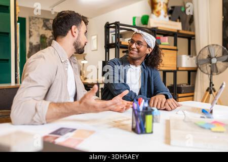 Two coworkers engaged in a lively discussion at a modern coworking space, exchanging ideas and collaborating on a project, surrounded by a creative an Stock Photo