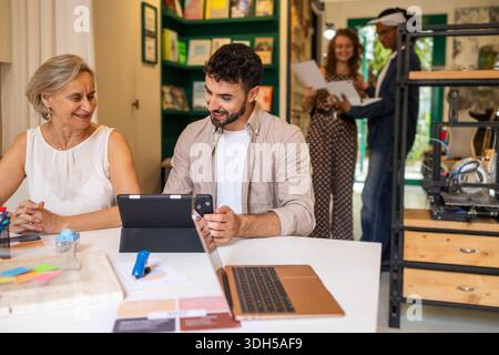 A diverse group of coworkers engaging in teamwork at a modern coworking space. Two individuals discuss a project, while two others collaborate in the Stock Photo
