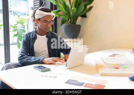 A young professional focused on work at a coworking space. The atmosphere is bright and modern, featuring a laptop, phone, and assorted office materia Stock Photo