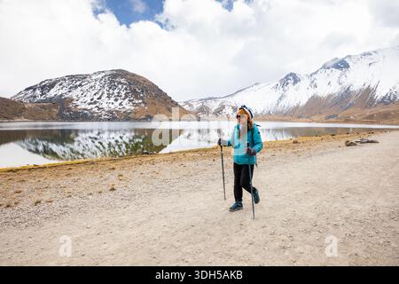 A mountain hiker walks along a serene lake with snowy peaks in the background. The group explores the alpine trail, showcasing a love for nature and a Stock Photo