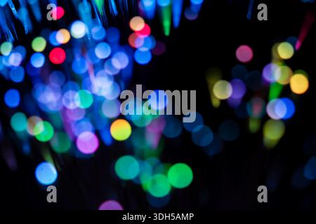 A captivating display of vibrant, multicolored fiber optic lights creating a stunning bokeh effect on a black background. The abstract pattern is mesm Stock Photo
