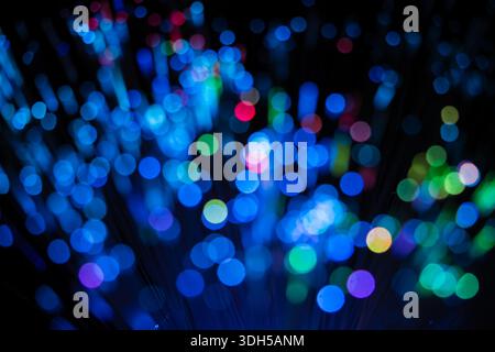 Abstract image featuring vibrant fiber optic lights with blue, green, and red bokeh effects against a black background, creating an ethereal and mesme Stock Photo