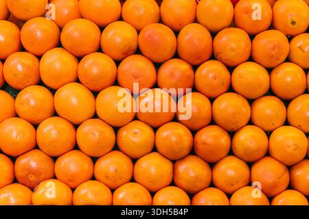 A vibrant display of fresh oranges neatly arranged on a green background at a market setting. These citrus fruits offer a burst of color and promise o Stock Photo