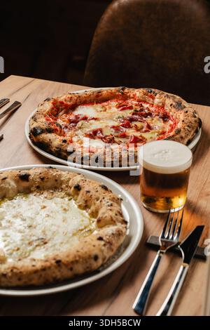 Two delicious pizzas on a wooden table in a cozy pizzeria setting. A perfect combination of crispy crust, melted cheese, and toppings complemented by Stock Photo