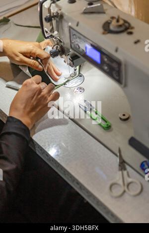 Asian Muslim woman seamstress working diligently on a handmade fabric design, showcasing her skills and creativity in a cozy home workshop environment Stock Photo