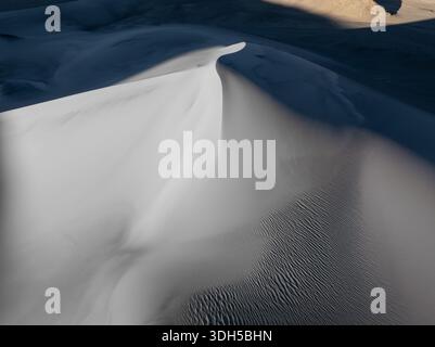 Serene white sand dunes display intricate textures, highlighting the artistry of nature. The soft curves and delicate patterns create a breathtaking d Stock Photo