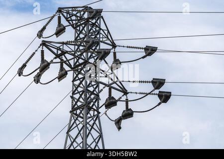 A detailed low angle view of a high voltage electric transmission tower with multiple power lines contrasted against a cloudy sky, representing energy Stock Photo