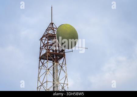 A tall satellite communication tower with a distinctive green dish stands against a clear blue sky, showcasing telecom technology and infrastructure e Stock Photo