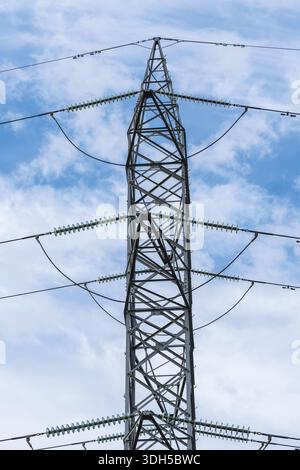 A towering high voltage transmission tower stretches into a clear blue sky, showcasing its metal lattice framework. The power lines extend outward, il Stock Photo