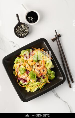 A vibrant salad featuring iceberg lettuce, carrots, and radicchio, topped with fried shrimp. Garnished with cilantro and sesame seeds, served with soy Stock Photo