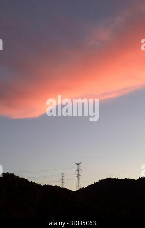 Twilight descends as power lines stretch across the silhouette of hills, set against a vibrant pink and purple sky, capturing the tranquil beauty of n Stock Photo