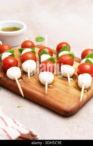Fresh skewers featuring cherry tomatoes, mozzarella balls, and basil leaves elegantly arranged on a wooden board, perfect for a delightful appetizer p Stock Photo