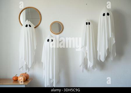 Elegant Halloween decorations feature floating ghost figures with spooky black eyes paired with small pumpkins on a shelf, creating a festive and eeri Stock Photo