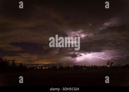 A breathtaking image captures a bright lightning bolt illuminating a dark and stormy sky over a cityscape. The electric discharge creates a dramatic c Stock Photo