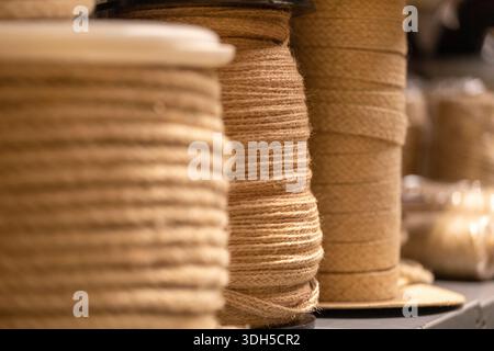 Close up of several large spools of natural brown twine neatly wound and lined up on shelves in a workshop setting. The texture and fibers are visible Stock Photo
