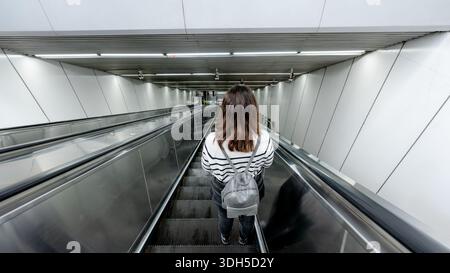 A woman descends an empty escalator in a modern Beijing subway station, showcasing the sleek design and daily commute in the bustling city of Beijing, Stock Photo
