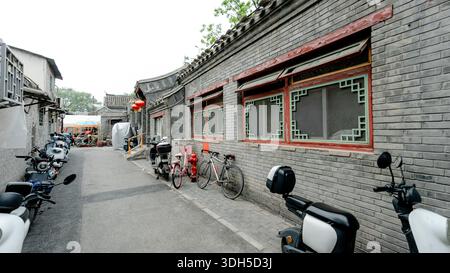 Scenic view of a traditional hutong in Beijing, China, featuring parked bicycles and scooters against historic gray brick buildings. Quiet ambiance an Stock Photo