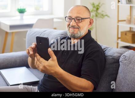 Smiling senior man using smartphone on sofa at home during video call session Stock Photo