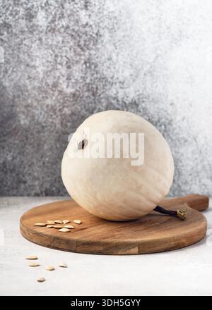 White "Snowball" squash (Cucurbita pepo) with smooth white rind and scattered seeds on wooden board. Ideal for food photography, gardening and season. Stock Photo