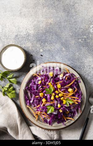 A fresh, colorful vegan slaw made with shredded red cabbage, grated carrot, and corn, served with yogurt dressing on a rustic stone surface. garnished Stock Photo