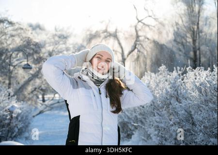Portrait of smiling woman in snowy forest wearing warm clothes, concept of happiness, nature and winter lifestyle Stock Photo