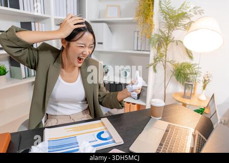Stressed businesswoman dealing with heavy work pressure, reacting emotionally while reviewing reports and facing tight deadlines, highlighting workpla Stock Photo