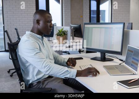 African American man working on spreadsheet on external monitor at modern office, copy space Stock Photo