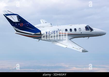 Cessna 525 CitationJet M2 business jet aircraft registration YU-SCM with serial number 525-0918 is shown in flight from a close pilot perspective during an air-to-air photography session. The light corporate jet is powered by two Williams International FJ44-1AP-21 turbofan engines and features modern avionics and swept wings. The aircraft appears clean and well maintained while operating over Serbia during the Serbian Airpower 2025 aviation event with clear sky conditions and stable cruise flight. Stock Photo