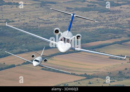This image shows two business jets operated by Prince Aviation flying in close formation during an air-to-air photography flight at Serbian Airpower 2025. The aircraft include a Cessna 525 CitationJet M2, registration YU-SCM, serial number 525-0918, and a Cessna 560XL Citation XLS, registration YU-SVL, serial number 560-5772. The CitationJet M2 is a light jet powered by two Williams FJ44-1AP-21 turbofan engines. The Citation XLS is a midsize jet equipped with two Pratt & Whitney Canada PW545C turbofan engines. The close-up pilot view highlights cockpit windows, fuselage alignment, and stable f Stock Photo