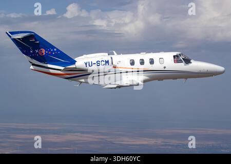 This image presents a close-up air-to-air view of a Cessna 525 CitationJet M2 operated by Prince Aviation during Serbian Airpower 2025. The aircraft carries registration YU-SCM and serial number 525-0918. The CitationJet M2 is a light business jet designed for short to medium range operations and is powered by two Williams FJ44-1AP-21 turbofan engines. The view emphasizes the cockpit area, pilot seating position, forward fuselage, and wing root while the aircraft maintains steady flight. The photograph documents the aircraft’s exterior configuration and operational presence at the aviation eve Stock Photo
