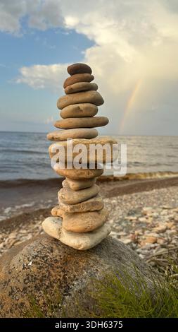 Balanced stones stacked on the shore with a rainbow in the background Stock Photo