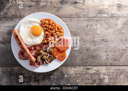 Full English breakfast with fried egg, bacon, sausages and beans on wooden table Stock Photo