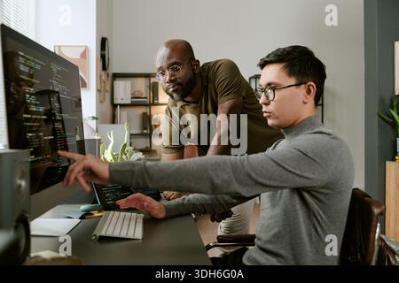 Young Asian Man Collaborating with Young Black Man While Coding Software Stock Photo