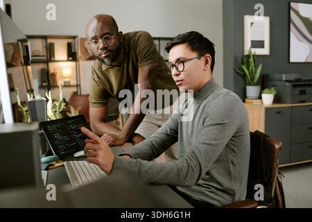 Young Man Explaining Code to Young Black Man in Office Setting Stock Photo