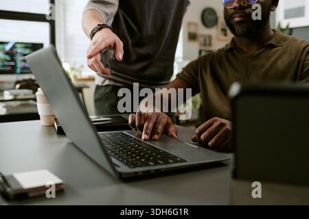 Young Black Man Using Laptop While Colleague Pointing at Screen Stock Photo