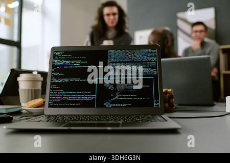 Young Adult Men Collaborating in Office While Laptop Displaying Programming Code Stock Photo