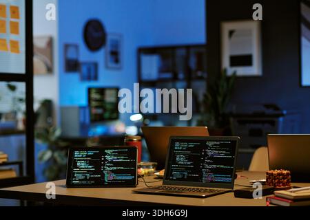 Laptop Computers Displaying Programming Code in Modern Office at Night Stock Photo