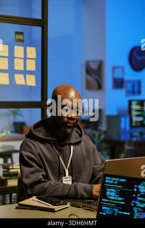 Young Black Man Working on Laptop in Modern Office at Night Stock Photo