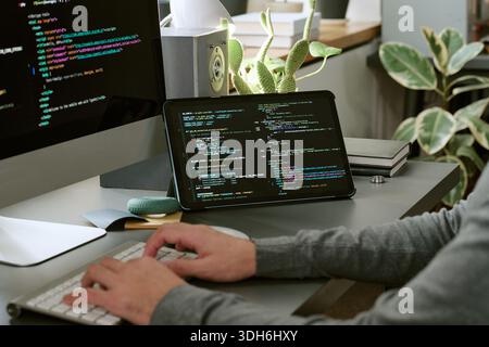 Unrecognizable Man Coding Software on Computer and Tablet in Office Stock Photo