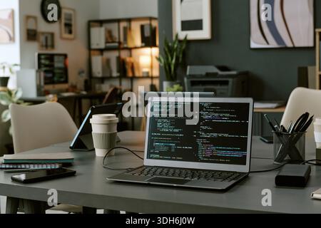 Modern Office Workspace Featuring Laptop Displaying Programming Code on Screen Stock Photo