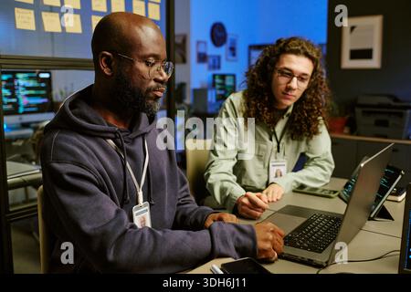 Young Black Man and Young Caucasian Man Collaborating on Laptop in Office Stock Photo