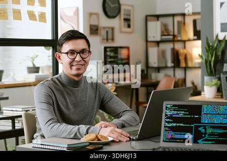 Portrait of Young Adult Man Smiling While Working on Laptop in Office Stock Photo