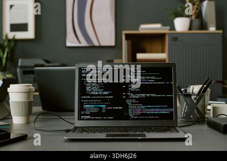 Laptop Displaying Programming Code on Office Desk during Software Development Stock Photo