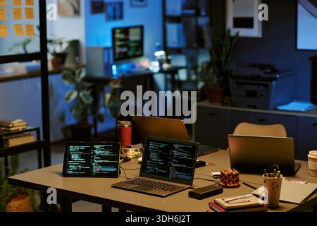 Empty Office Workspace Featuring Multiple Laptops Displaying Programming Code Stock Photo
