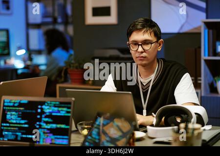 Young Adult Man Working on Laptop in Modern Office at Night Stock Photo
