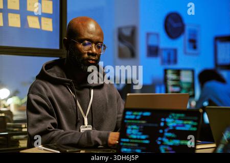 Young Black Man Concentrating on Software Engineering Task at Night Office Stock Photo